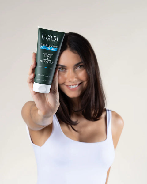 Woman holding a Luxeol shampoo bottle against a plain background