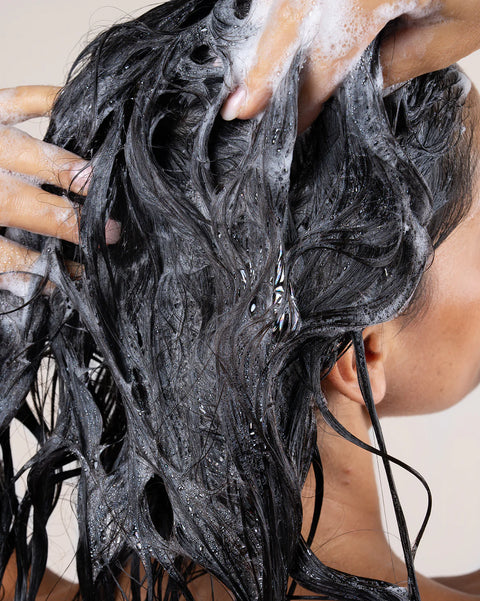Person washing black hair with soapy hands against a neutral background