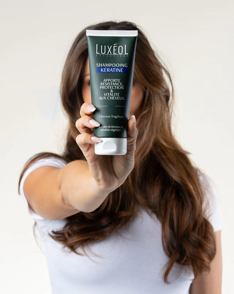 Person holding a Luxeol shampoo bottle with a plain background