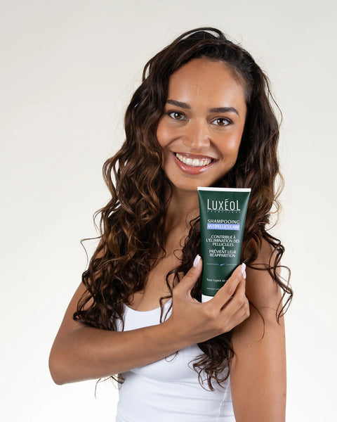 Woman holding a tube of Luxeol shampoo against a white background