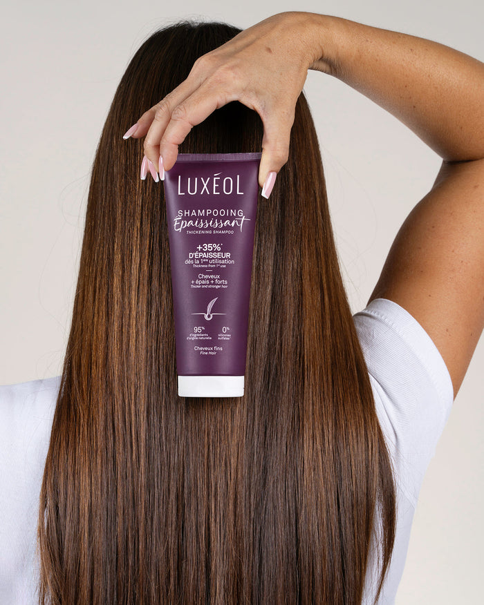 Person holding a Luxéol shampoo bottle with long, straight hair.